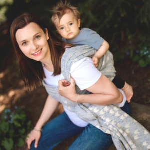 Mama nosząca dziecko w chuście na świeżym powietrzu, oboje uśmiechnięci i zrelaksowani.